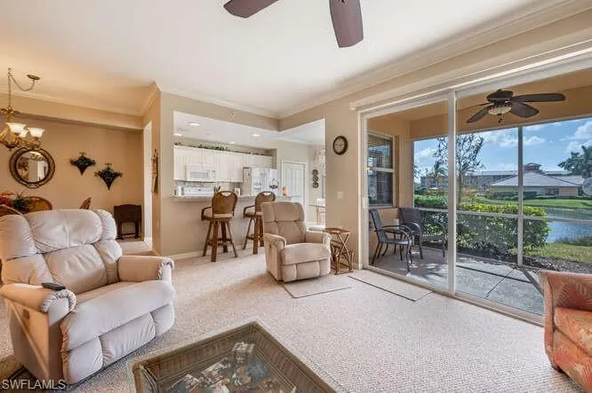 Carpeted living room featuring ornamental molding, a water view, and ceiling fan with notable chandelier