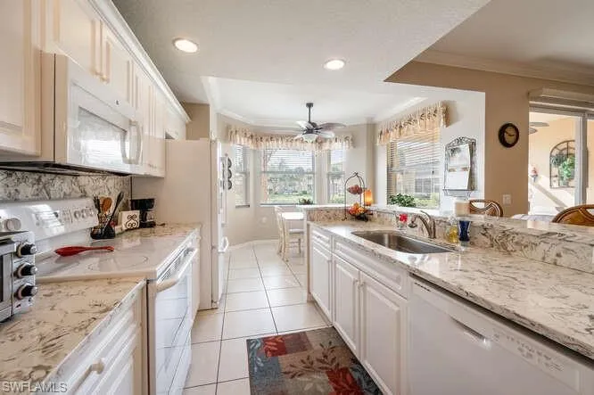 Kitchen featuring white appliances, light tile patterned floors, white cabinetry, and ornamental molding