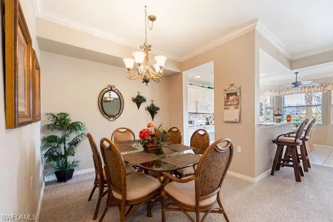 Carpeted dining space with crown molding and ceiling fan with notable chandelier