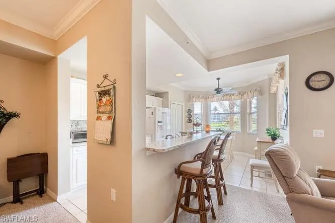 Kitchen featuring white fridge with ice dispenser, a kitchen bar, white cabinetry, light stone counters, and ornamental molding