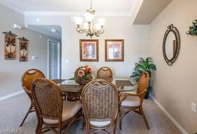 Carpeted dining area featuring crown molding and a chandelier