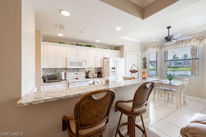Kitchen with white appliances, light stone countertops, backsplash, ceiling fan, and white cabinets