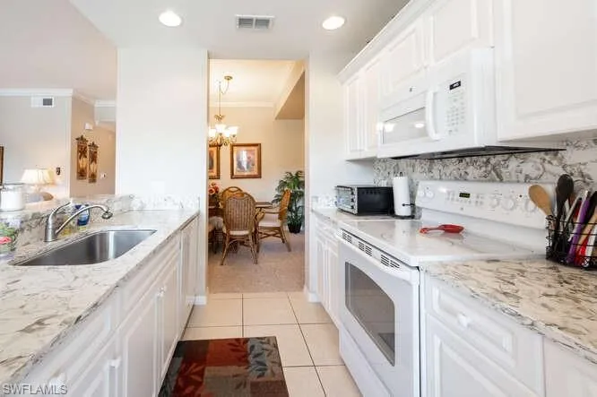 Kitchen with ornamental molding, sink, a notable chandelier, white electric range oven, and white cabinets