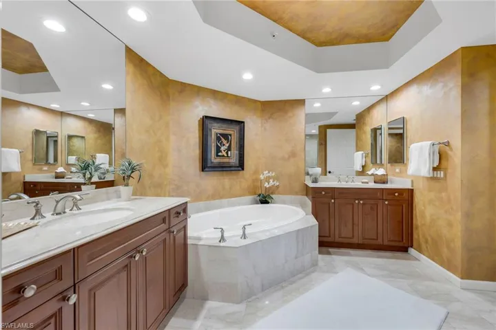 Primary bath with marble counters, floor, & tub surround. Separate shower and tray ceiling.