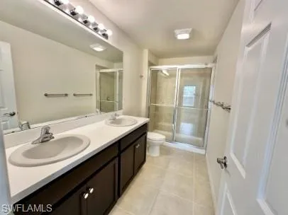 Spacious bathroom featuring a dual-sink vanity with dark wood-finish cabinetry, a large vanity mirror, a glass-enclosed shower, and light-toned tile flooring