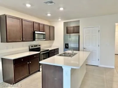 Modern kitchen featuring an island with an undermount sink, dark wood-finish cabinetry, light countertops, stainless steel appliances, and recessed lighting