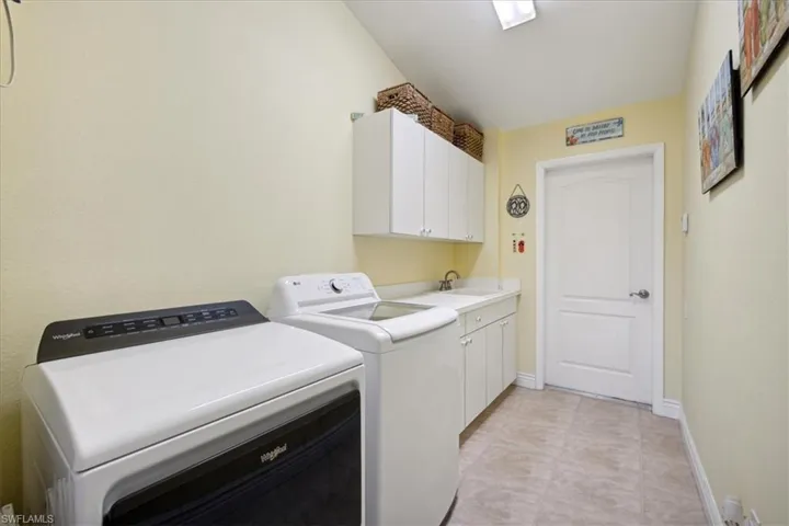 Laundry room featuring washer and clothes dryer, sink, light tile flooring, and cabinets