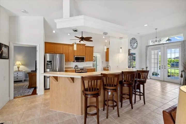 Kitchen featuring french doors, appliances with stainless steel finishes, a kitchen bar, ceiling fan, and light tile floors