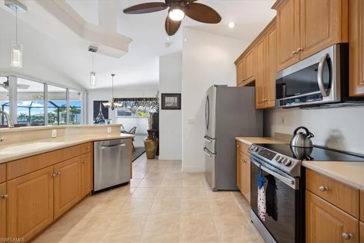 Kitchen with stainless steel appliances, ceiling fan with notable chandelier, light tile floors, hanging light fixtures, and sink