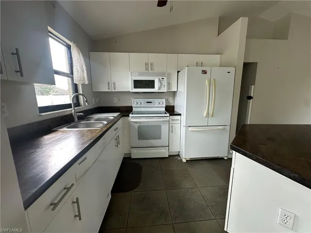 Kitchen with white cabinets, white appliances, lofted ceiling, dark tile patterned flooring, and sink