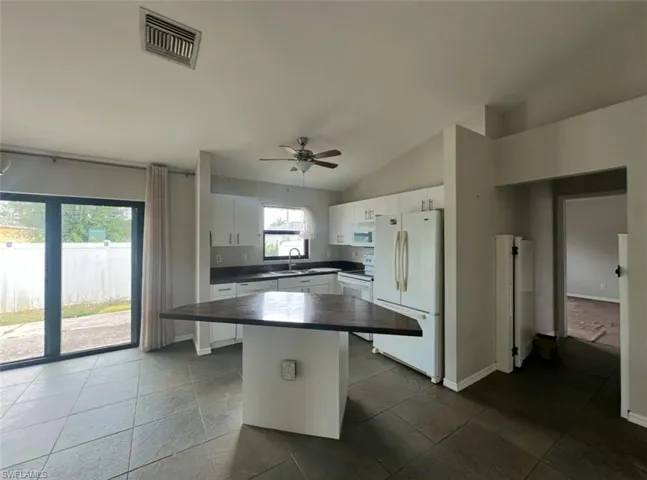 Kitchen featuring a center island, a sink, white appliances, dark countertops, and white cabinets
