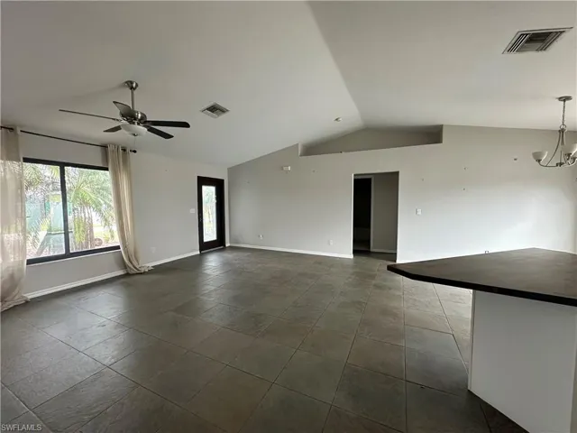 Unfurnished room with lofted ceiling and ceiling fan with notable chandelier