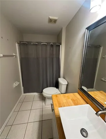 Bathroom with tile patterned floors, vanity, toilet, and curtained shower