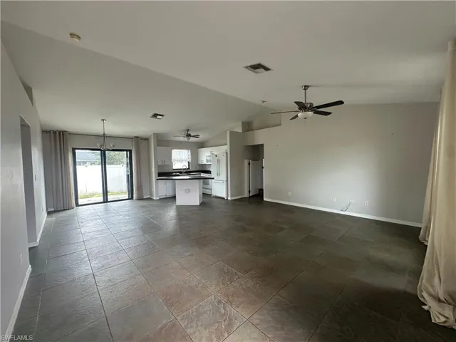 Unfurnished living room with ceiling fan with notable chandelier and vaulted ceiling