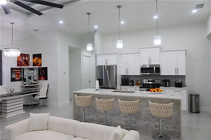 Kitchen with a high ceiling, open floor plan, stainless steel appliances, a breakfast bar, and light stone counters