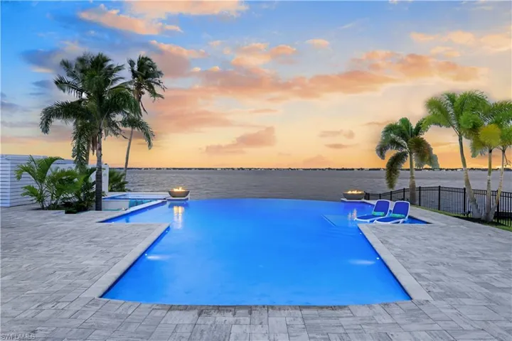 Pool at dusk with a water view, a pool with connected hot tub, and a patio