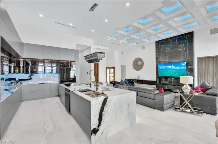 Kitchen featuring modern cabinets, gray cabinetry, coffered ceiling, a center island with sink, and light stone counters