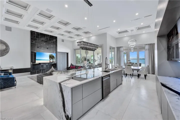 Kitchen featuring modern cabinets, coffered ceiling, light stone counters, gray cabinetry, and a kitchen island with sink