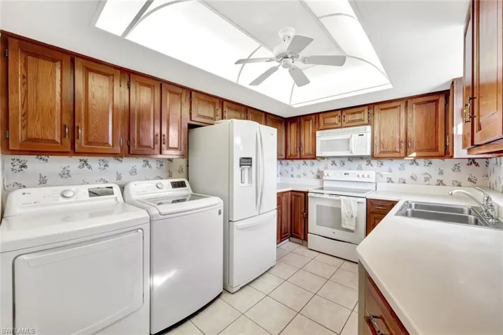 Kitchen with light tile patterned flooring, washer and dryer, sink, ceiling fan, and white appliances