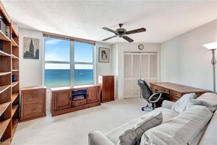 Home office featuring a water view, light colored carpet, ceiling fan, and a textured ceiling