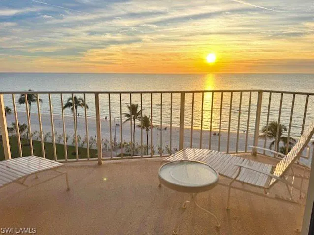 Balcony at dusk featuring a water view and a view of the beach