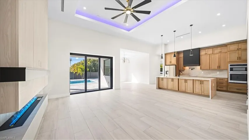 Kitchen featuring open floor plan, a tray ceiling, decorative backsplash, a chandelier, and a large island with sink