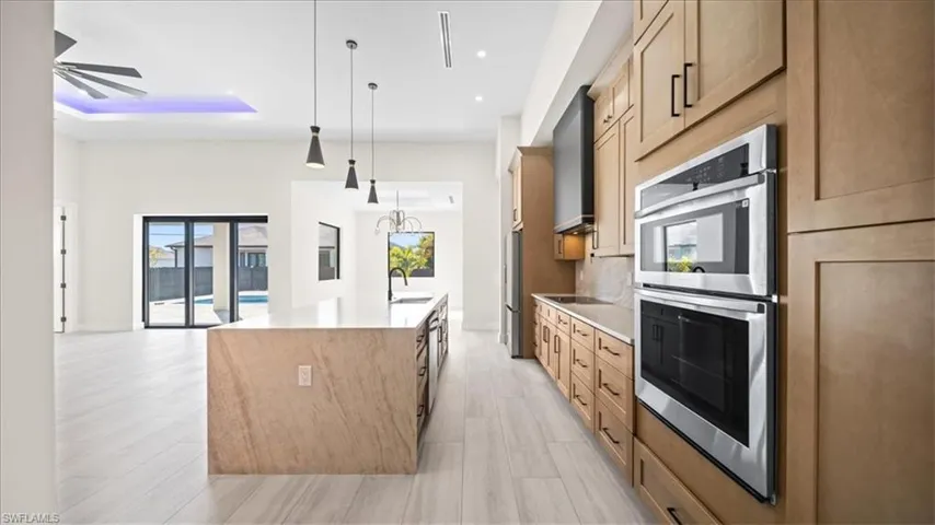 Kitchen with double oven, light stone countertops, a spacious island, and light wood-style flooring