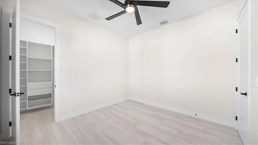 Unfurnished bedroom featuring a walk in closet, light wood-style floors, and a ceiling fan