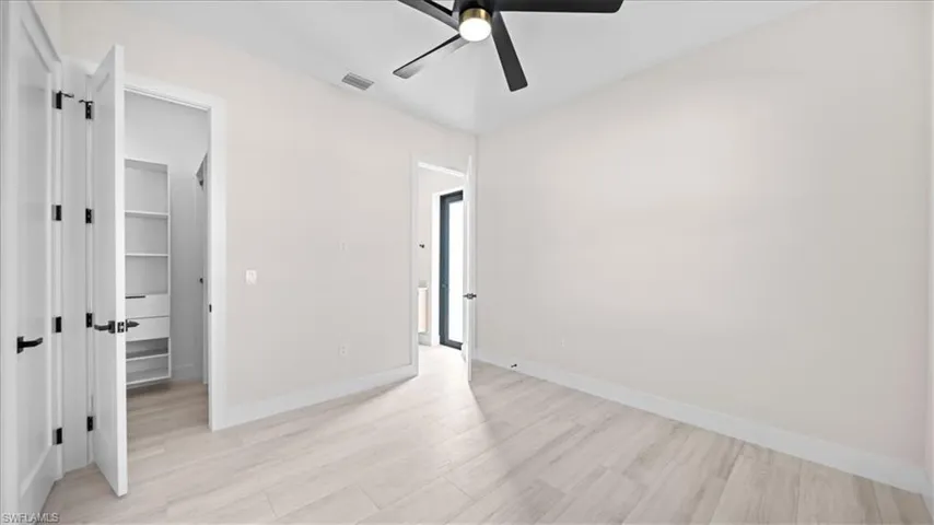 Unfurnished bedroom with a spacious closet, light wood-style flooring, and ceiling fan