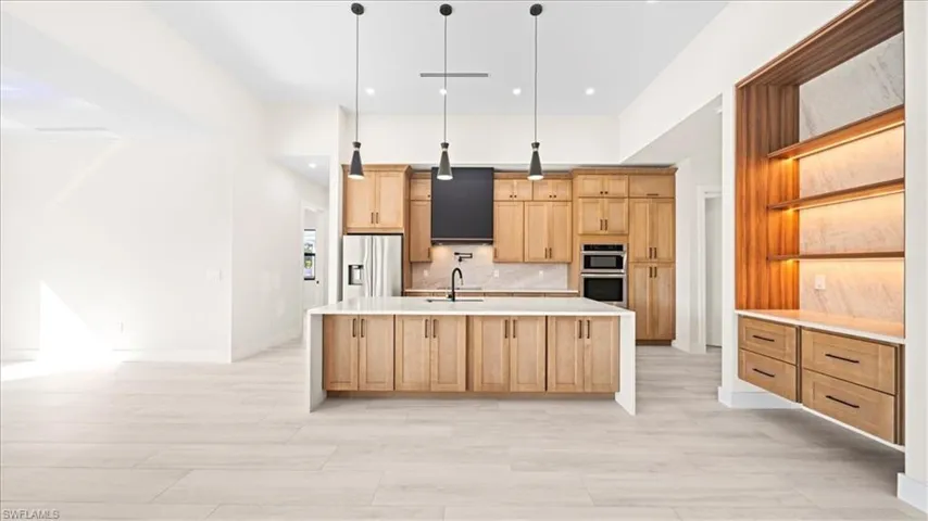 Kitchen featuring a large island, open shelves, decorative light fixtures, light wood finish cabinetry, and stainless steel appliances
