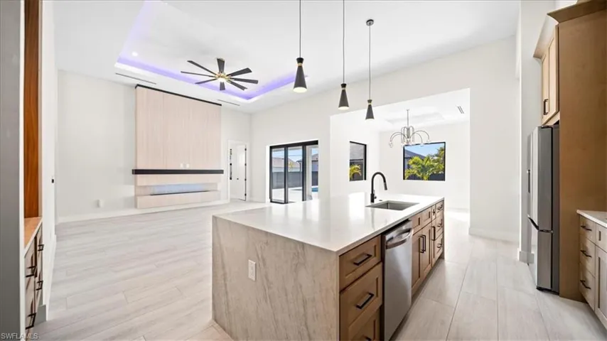 Kitchen with a raised ceiling, open floor plan, light stone counters, freestanding refrigerator, and a center island with sink