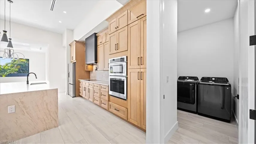 Kitchen with light wood finish cabinets, stainless steel appliances, washer and clothes dryer, decorative backsplash, and light stone counters
