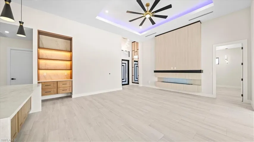 Unfurnished living room featuring light wood finished floors, a ceiling fan, a tray ceiling, and built in features