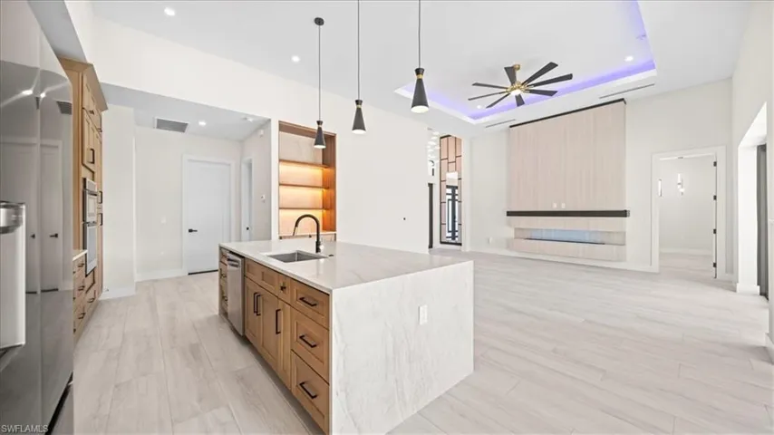 Kitchen featuring light stone counters, stainless steel appliances, a tray ceiling, open floor plan, and an island with sink