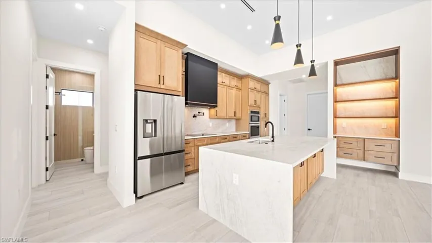 Kitchen with light wood finish cabinets, stainless steel appliances, an island with sink, and light stone countertops