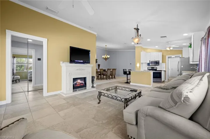 Living area with a ceiling fan, recessed lighting, crown molding, a warm lit fireplace, and a chandelier