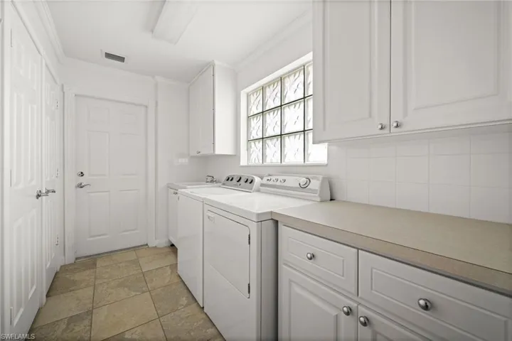 Washroom featuring ornamental molding, independent washer and dryer, and cabinet space