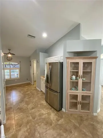 Kitchen with stainless steel fridge, vaulted ceiling, white cabinetry, a ceiling fan, and glass insert cabinets