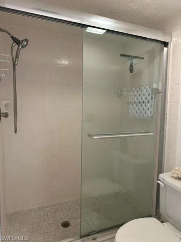 Glass-enclosed shower featuring a handheld showerhead and light-toned square tile walls