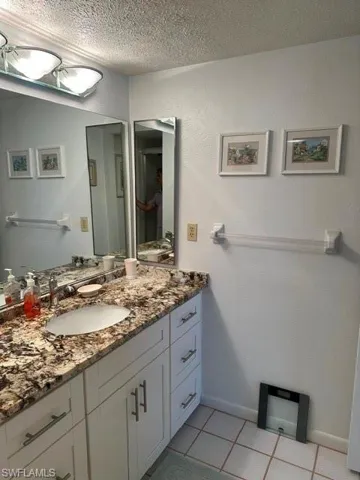 Bathroom vanity featuring an integrated sink, granite-style countertop, white cabinetry with brushed nickel hardware, and tile flooring
