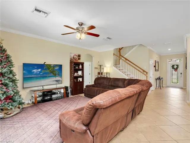 Living room with ornamental molding, light tile patterned flooring, ceiling fan, stairs, and arched walkways