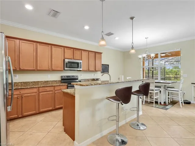 Kitchen with a kitchen breakfast bar, light tile patterned floors, ornamental molding, appliances with stainless steel finishes, and dark stone countertops