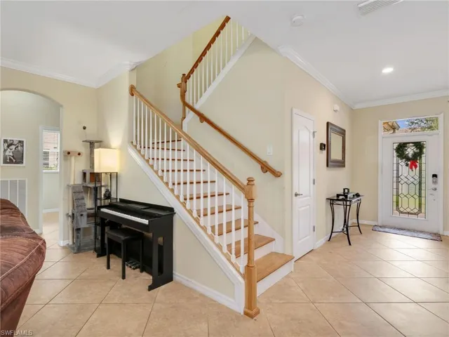 Foyer featuring crown molding, light tile patterned floors, stairway, and arched walkways