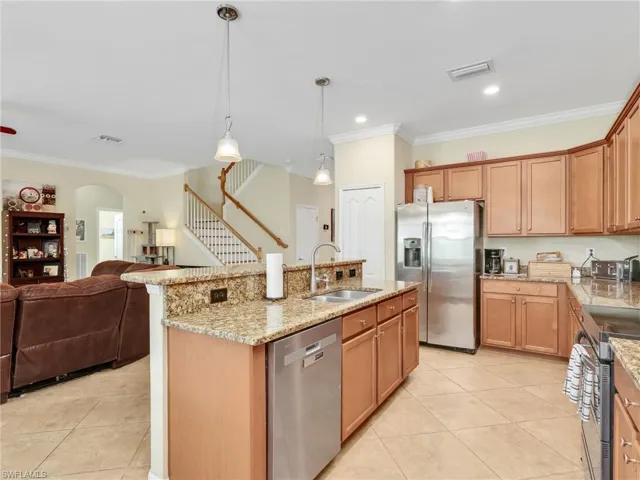 Kitchen with ornamental molding, light stone countertops, appliances with stainless steel finishes, pendant lighting, and a kitchen island with sink