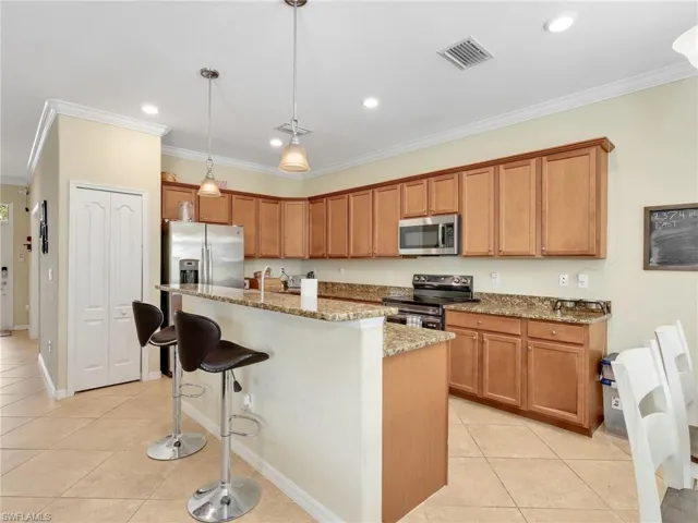 Kitchen featuring light stone countertops, a breakfast bar area, light tile patterned floors, appliances with stainless steel finishes, and crown molding