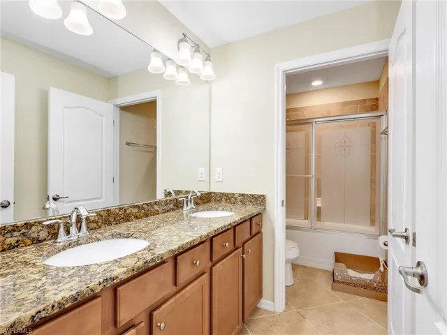 Full bathroom featuring double vanity, shower / bath combination with glass door, and light tile patterned floors
