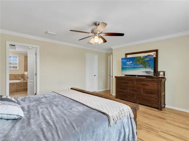 Bedroom with crown molding, light wood-style floors, a ceiling fan, and ensuite bathroom