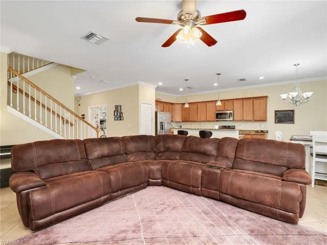 Living area with light tile patterned floors, crown molding, a ceiling fan, a chandelier, and stairs