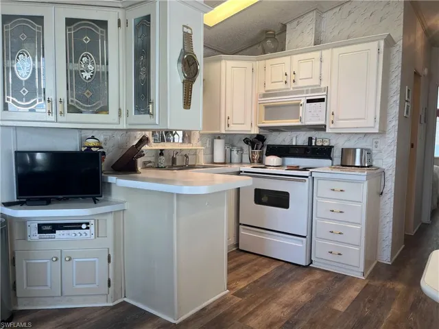 Kitchen featuring light countertops, white appliances, dark wood-style flooring, a peninsula, and white cabinets
