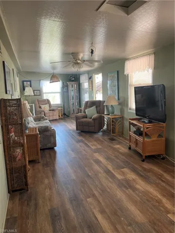 Living room with healthy amount of natural light, dark wood-type flooring, ceiling fan, and a textured ceiling
